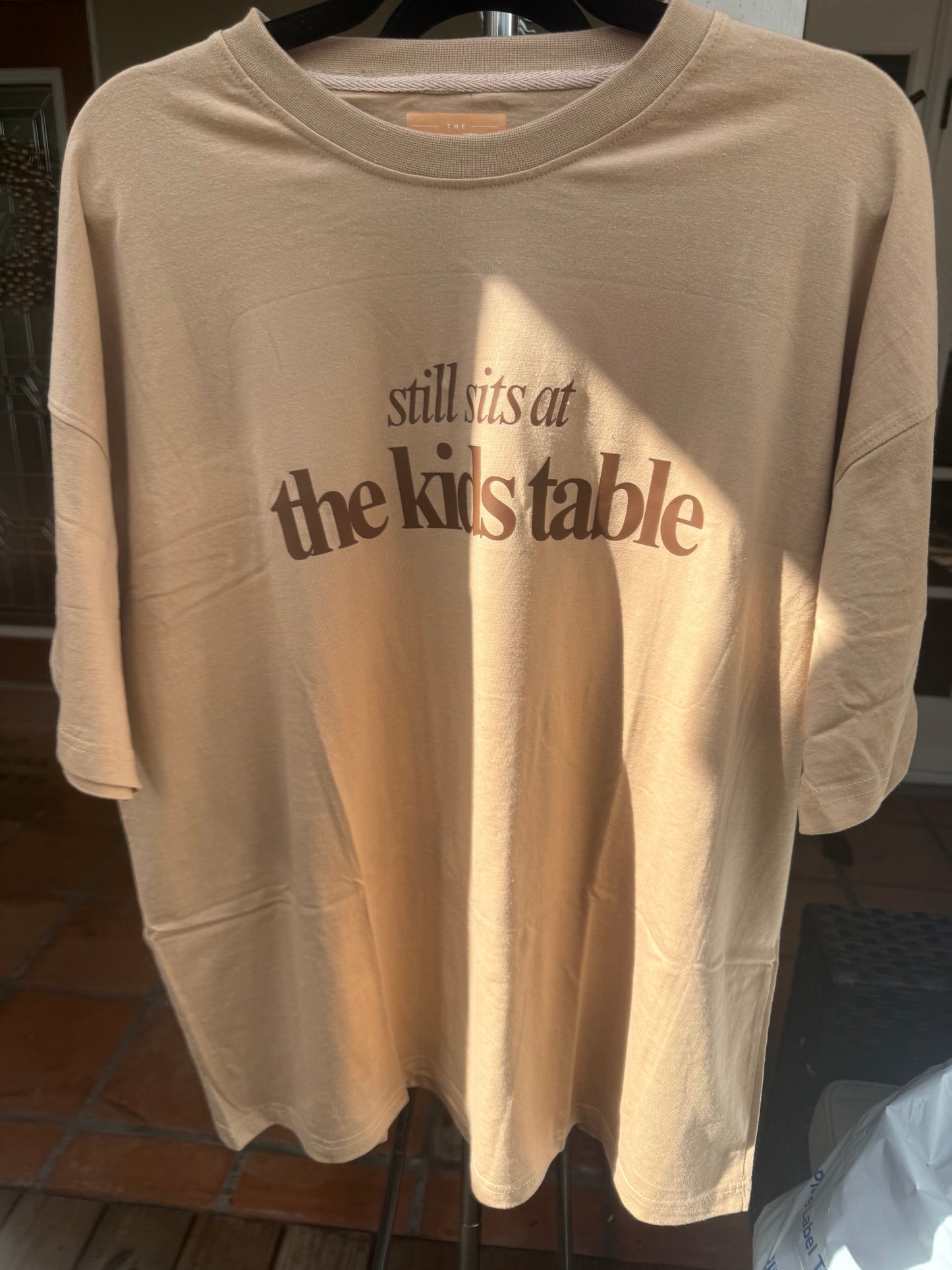 Tan “Still Sits at the Kids Table” Thanksgiving Oversized Tee – Soft Drop-Shoulder Unisex Shirt