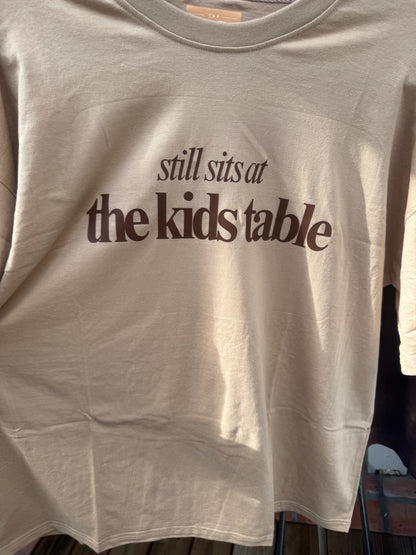 Tan “Still Sits at the Kids Table” Thanksgiving Oversized Tee – Soft Drop-Shoulder Unisex Shirt