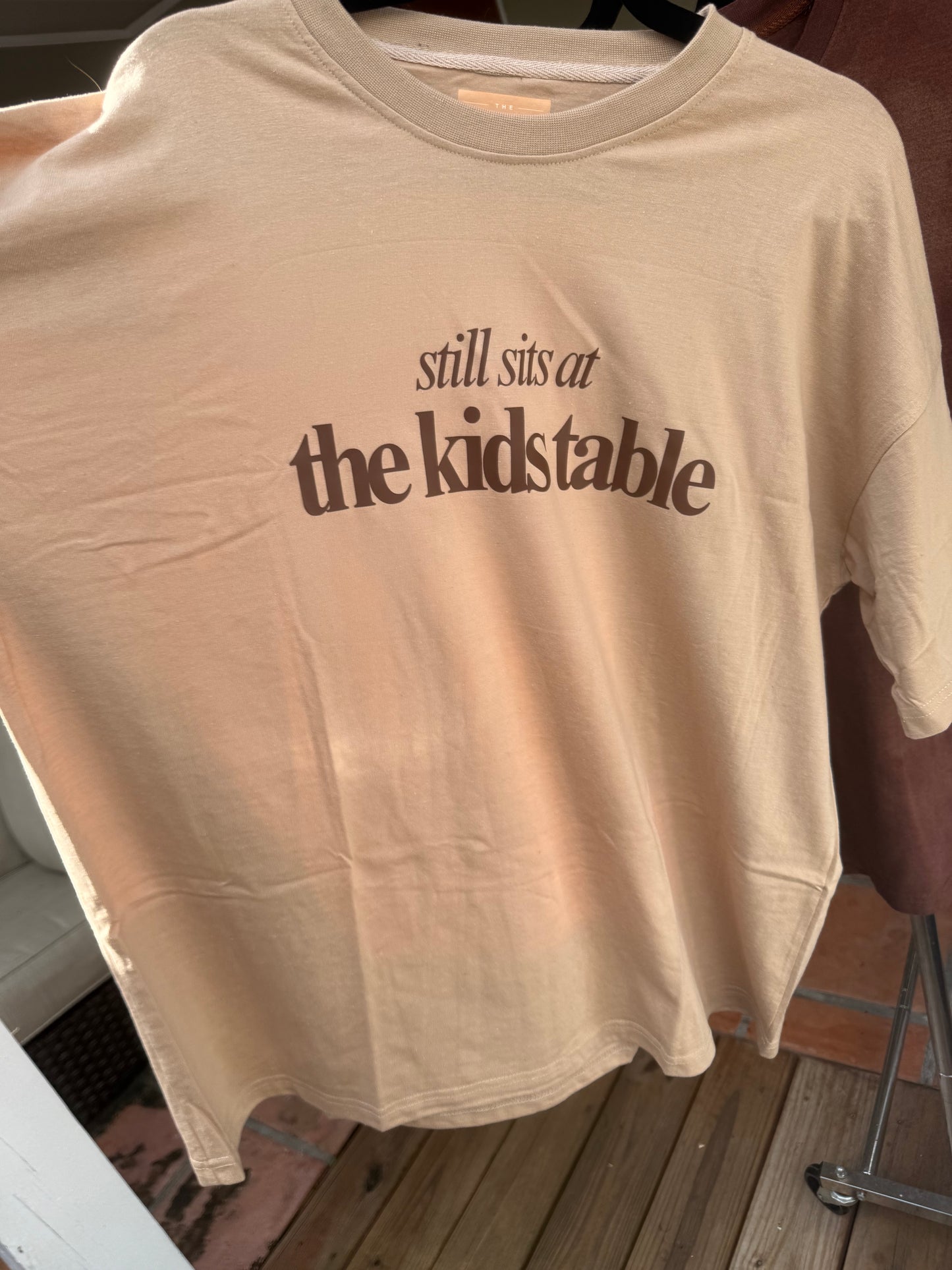Tan “Still Sits at the Kids Table” Thanksgiving Oversized Tee – Soft Drop-Shoulder Unisex Shirt