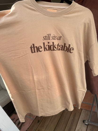 Tan “Still Sits at the Kids Table” Thanksgiving Oversized Tee – Soft Drop-Shoulder Unisex Shirt