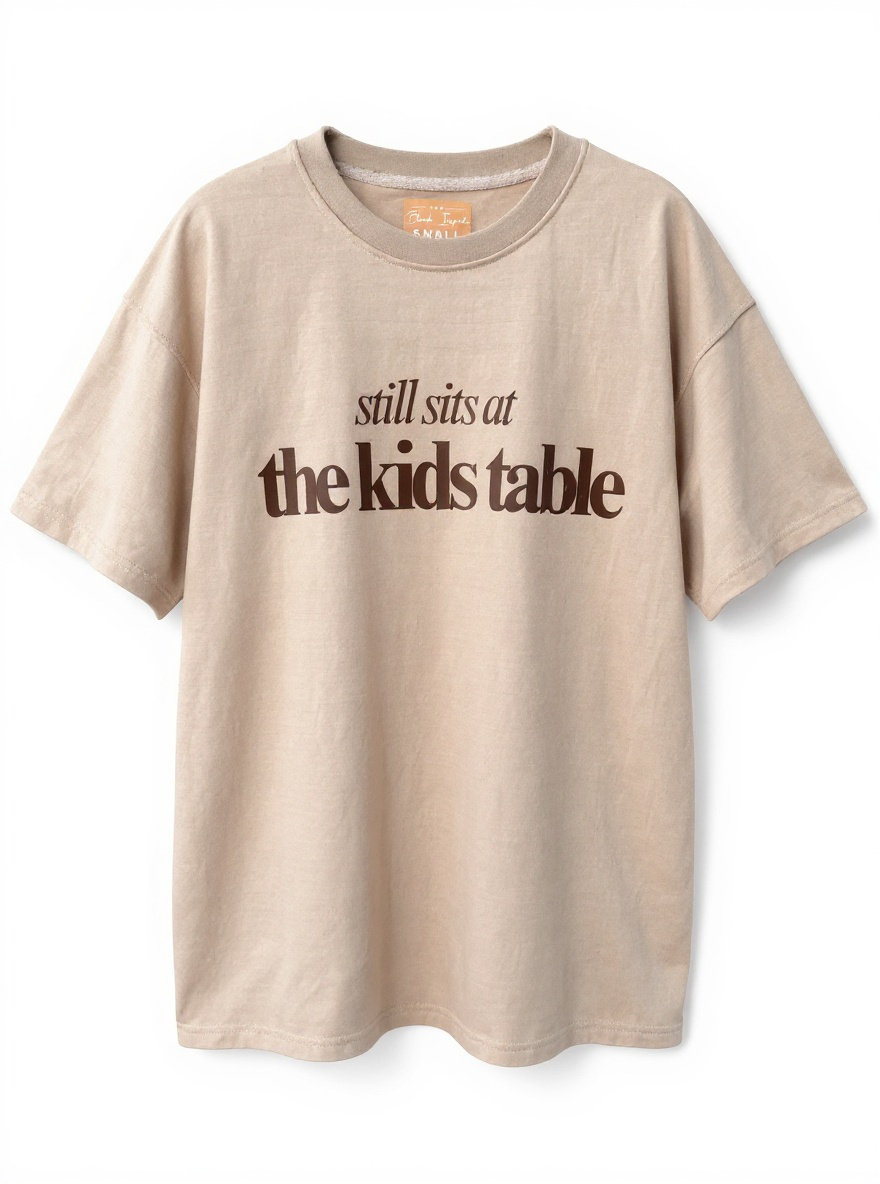 Tan “Still Sits at the Kids Table” Thanksgiving Oversized Tee – Soft Drop-Shoulder Unisex Shirt