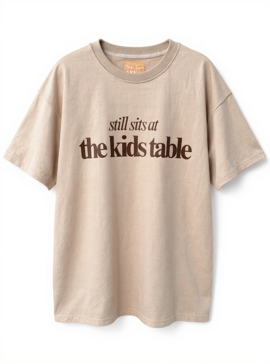 Tan “Still Sits at the Kids Table” Thanksgiving Oversized Tee – Soft Drop-Shoulder Unisex Shirt